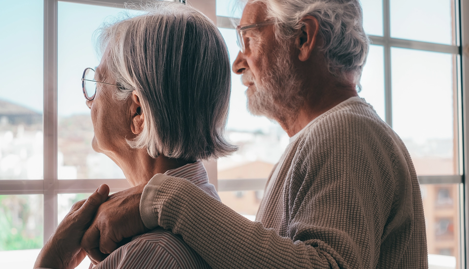 Dos personas mayores pensativas mirando por la ventana, simbolizando la planificación cuidadosa de la herencia.