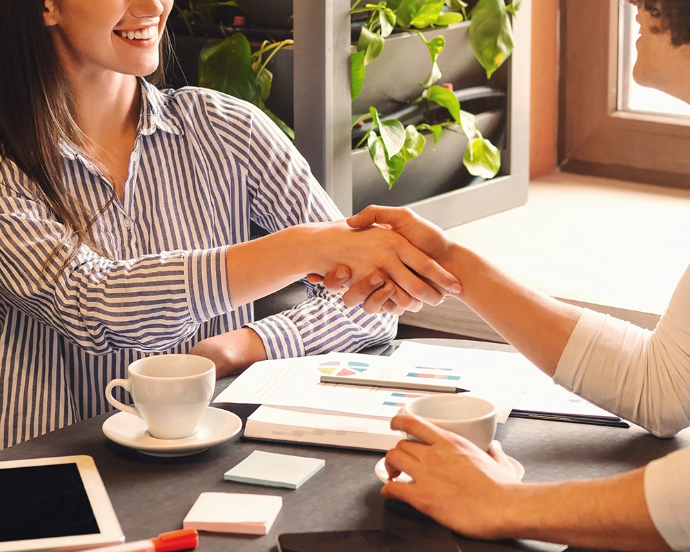 Imagen recortada de dos personas dándose un apretón de manos como símbolo de acuerdo y compromiso tras una reunión empresarial.