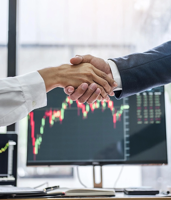 Cierre de un acuerdo profesional representado por un apretón de manos frente a una pantalla con gráficos de datos.