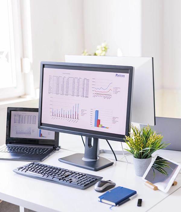 Mesa de trabajo con ordenador de sobremesa, portátil y tablet; en las pantallas se muestran estadísticas y gráficos de datos.