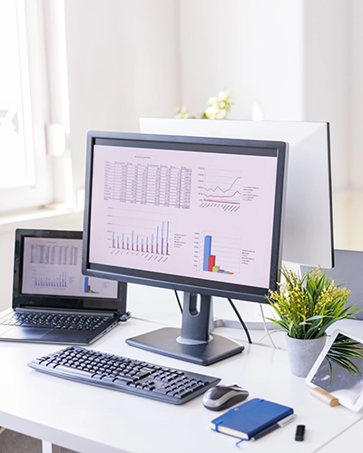Mesa de trabajo con ordenador de sobremesa, portátil y tablet; en las pantallas se muestran estadísticas y gráficos de datos.
