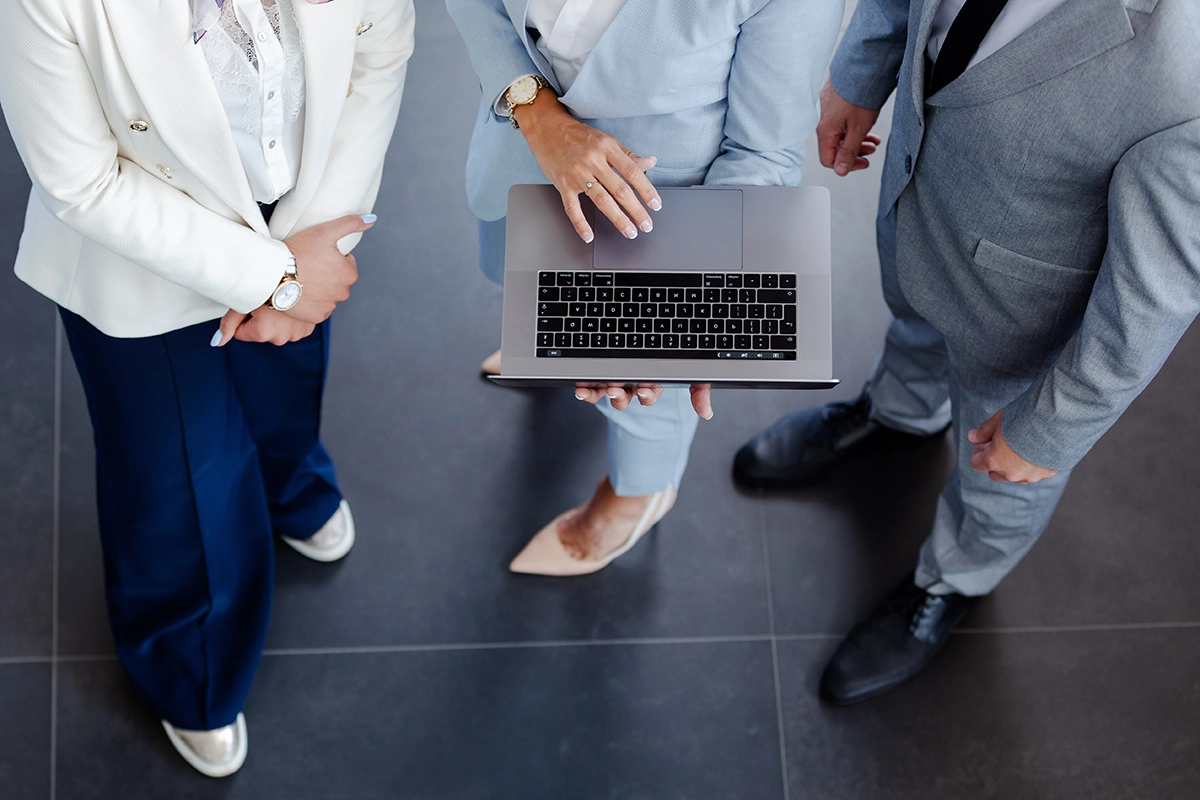 Vista aérea de un equipo de trabajo reunido alrededor de un portátil revisando información.